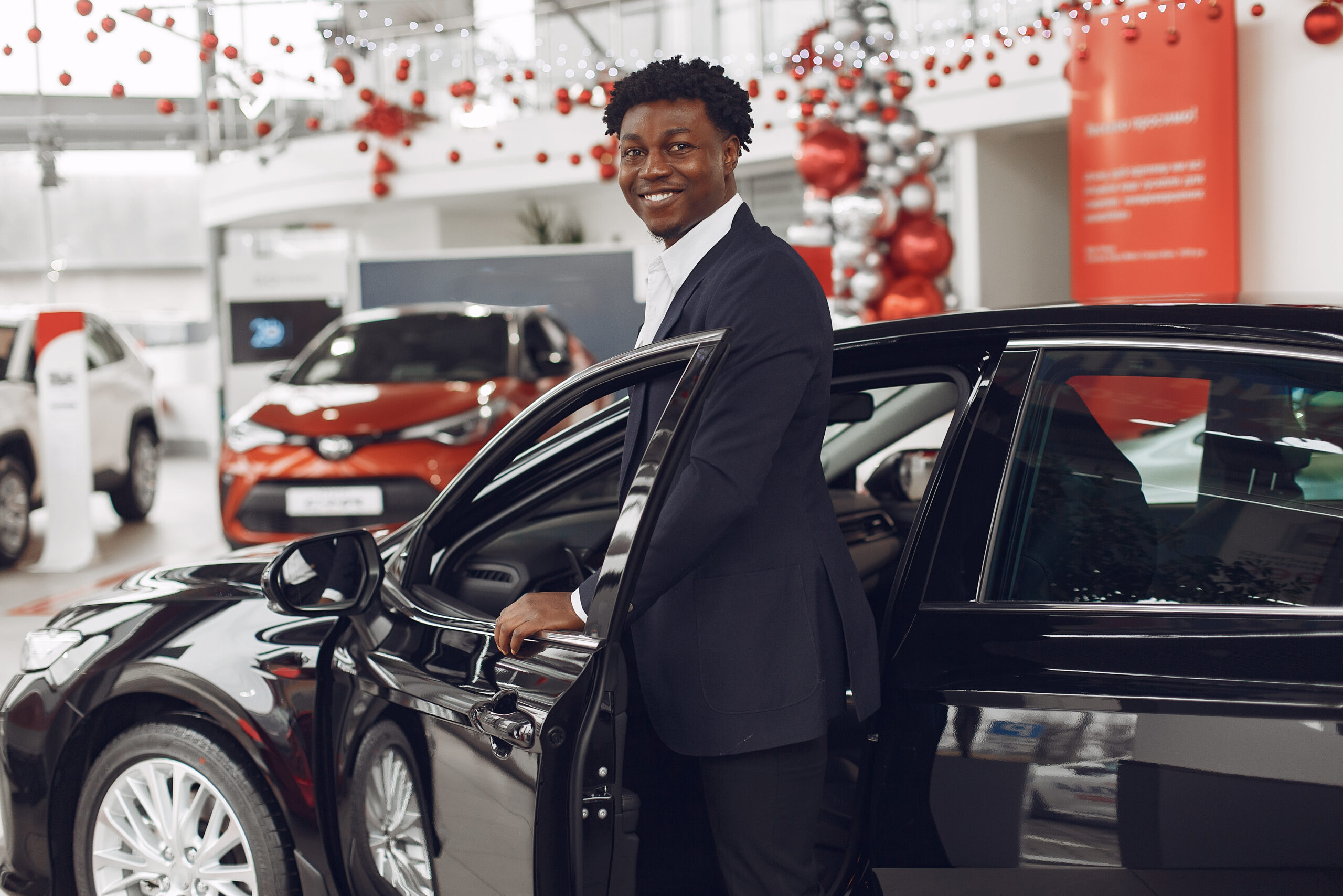 Man buying the car. Businessman in a car salon. Black male in a suit.